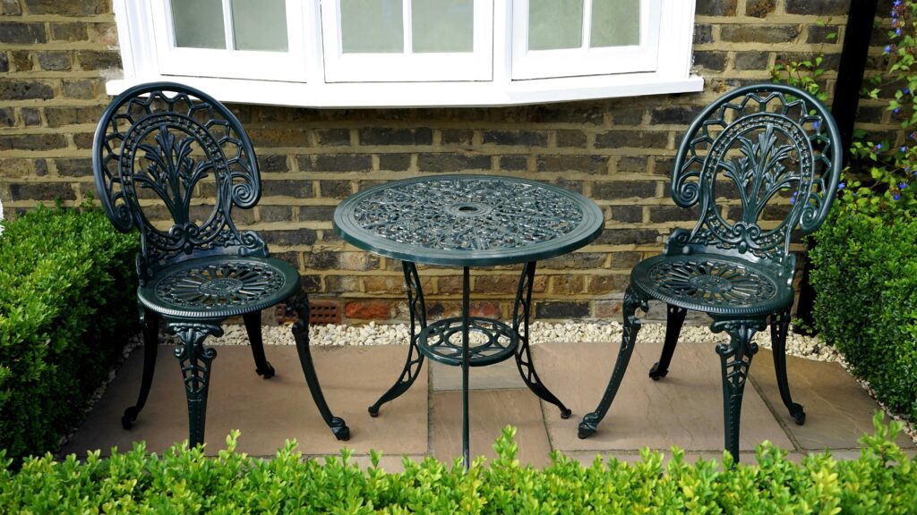 Elegant outdoor garden setting with vintage iron chairs and table beside a brick wall.